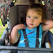 Brynnlee joined the competition — help win amazing prizes! toddler, child, stroller, blue_shirt, straps, floral_pattern, canopy, outdoor, greenery, curly_hair, rosy_cheeks, seat, resting_arm, daylight, casual_pose, young_child, portrait, baby_carriage, cute, expression