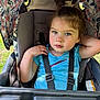 toddler, child, stroller, blue_shirt, straps, floral_pattern, canopy, outdoor, greenery, curly_hair, rosy_cheeks, seat, resting_arm, daylight, casual_pose, young_child, portrait, baby_carriage, cute, expression