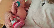 Elizabeth is registered to the contest to win money with this photo: newborn, baby, infant, child, adult, holding, pacifier, bottle, toy, sleepy, portrait, indoor, nursery, diapers, shelf, close_up, arms, curly_hair, white_shirt, family