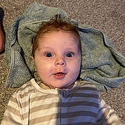 Kaleb joined the competition — help win amazing prizes! baby, infant, face, eyes, hair, towel, carpet, striped_clothing, onesie, floor, child, person, cute, expression, indoors, young_child, skin, portrait, lying_down, head