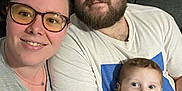 Kaleb is registered to the contest to win money with this photo: family, selfie, woman, man, baby, glasses, beard, couch, pillow, text, indoor, smile, happy, casual_clothing, striped_clothing, people, portrait, togetherness, home, cozy