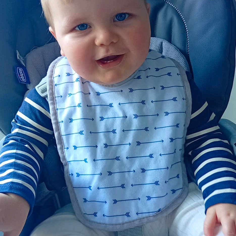 Eden a rejoint le concours — aidez-le/la à gagner de superbes lots ! baby, baby_bib, bib, blue_eyes, child, clothing, cute, face, feeding, furniture, happy, high_chair, indoor, infant, kitchen, person, seat, smile, striped_clothing, toes