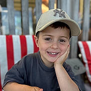 Naël a rejoint le concours — aidez-le/la à gagner de superbes lots ! child, boy, smile, baseball_cap, hat, face, portrait, hand_on_face, menu, table, striped_chair, wooden_fence, bokeh, eyes, teeth, casual_shirt, happy, sitting, restaurant, young_child