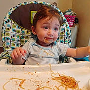 Otis is registered to the contest to win money with this photo: child, baby, high_chair, spaghetti, messy, food, meal, indoor, face, clothing, plate, tray, hair, blue_eyes, expression, sitting, cute, kitchen, dining, feeding
