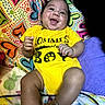 baby, infant, child, smiling, happy, portrait, indoors, bed, bedding, colorful, yellow_outfit, onesie, lying_down, sitting, face, hands, feet, pillow, heart_pattern, playful