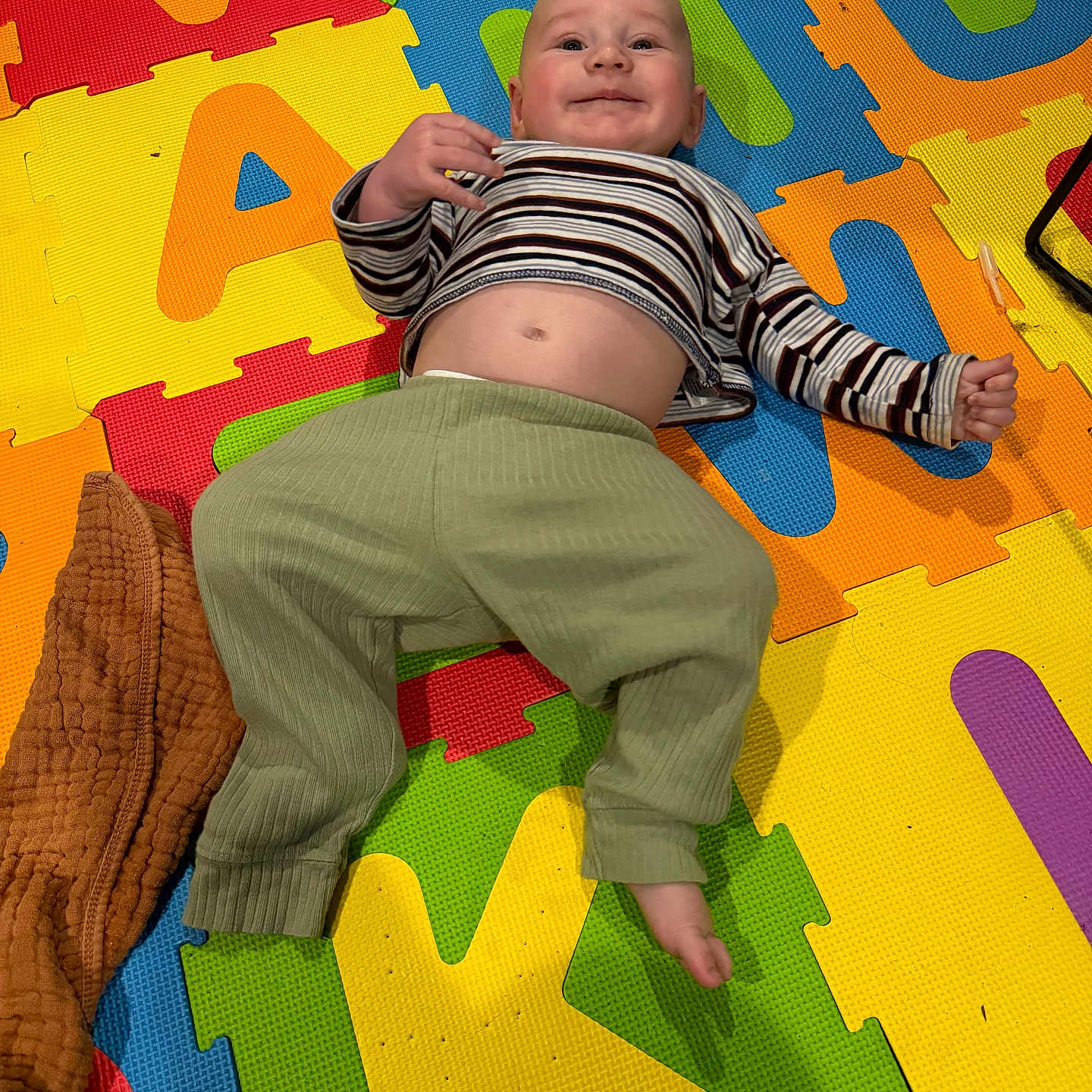 Noah joined the competition — help win amazing prizes! baby, infant, child, smiling, happy, lying_down, play_mat, alphabet_mat, colorful, indoor, portrait, face, striped_shirt, green_pants, barefoot, blanket, toys, floor, tummy, playroom
