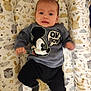 Samuel is registered to the contest to win money with this photo: baby, infant, child, sweater, mickey_mouse, clothing, lying_down, cushion, pattern, animal_print, indoor, person, cute, expression, baby_bed, soft_toys, black_pants, small_fists, face, head