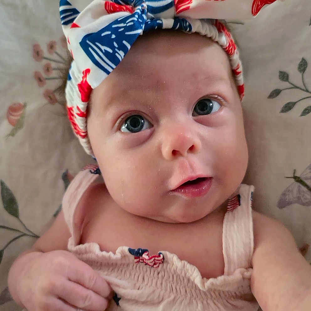 Abigail is registered to the contest to win money with this photo: baby, infant, face, headband, clothing, pink, blue, red, white, eyes, hand, portrait, cute, child, laying, blanket, pattern, skin, expression, soft