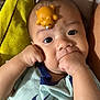 Mateo is registered to the contest to win money with this photo: baby, infant, face, hand, toy, rubber_bear, clothing, blue_shirt, skin, expression, cute, child, lying_down, cushion, yellow, closeup, indoors, portrait, sucking_fist, curious