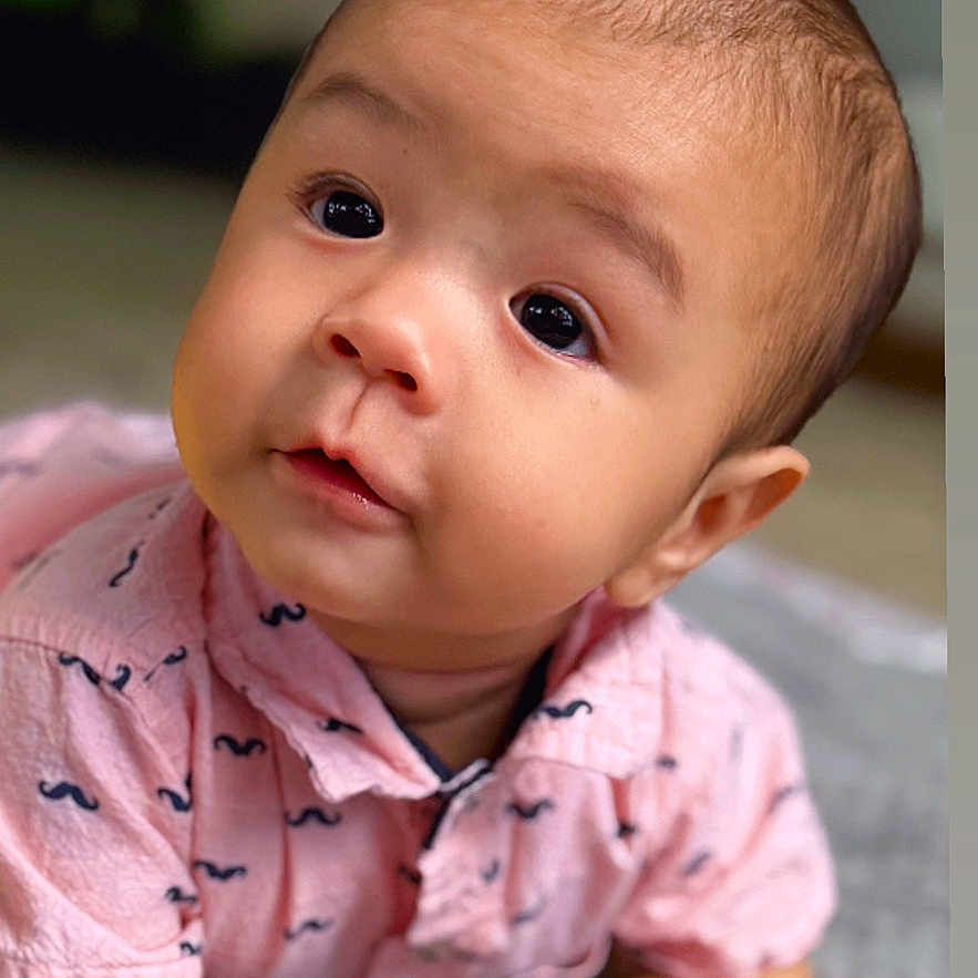 Mateo is registered to the contest to win money with this photo: adorable, baby, blanket, child, curious, cute, expression, eyes, face, hands, head, indoor, infant, lying_down, mustache_pattern, pink_shirt, portrait, skin, soft_texture, young