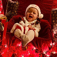 Jaina Willow joined the competition — help win amazing prizes! baby, child, smiling, santa_hat, christmas, holiday_lights, red_chair, wrapped_gifts, festive_clothing, indoors, celebration, joyful, cute, toddler, holiday_decor, seasonal, red, white, happy, portrait