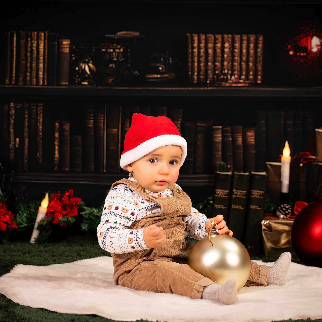 Nathan a rejoint le concours — aidez-le/la à gagner de superbes lots ! baby, bookshelf, candles, child, christmas_ornament, decorations, festive, gifts, gold, holiday, indoors, library, overalls, poinsettia, portrait, red, santa_hat, smiling, toddler, white_rug