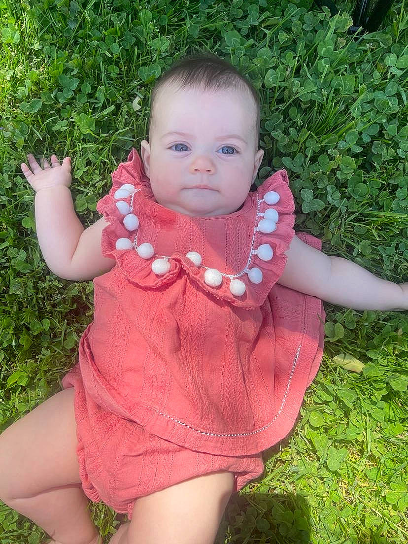 Aislynn is registered to the contest to win money with this photo: baby, baby_toddler_clothing, dress, finger, grass, grass_family, happy, human_body, leaf, lip, mouth, neck, pattern, people_in_nature, person, petal, pink, plant, skin, sleeve