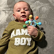 Mateo joined the competition — help win amazing prizes! baby, child, infant, toy, sweater, clothing, lying_down, soft_blanket, colorful_toy, hand, face, expression, indoor, cozy, cute, young_child, portrait, person, playful, mama_boy