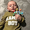 baby, child, infant, toy, sweater, clothing, lying_down, soft_blanket, colorful_toy, hand, face, expression, indoor, cozy, cute, young_child, portrait, person, playful, mama_boy