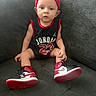 baby, child, sitting, couch, sneakers, headband, jersey, clothing, person, indoor, footwear, cute, sportswear, portrait, young_child, fashion, red, black, white, casual