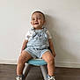 casual_clothing, chair, child, cute, fashion, footwear, happy, indoor, overalls, person, playful, portrait, shorts, sitting, smiling, sneakers, toddler, white_wall, wooden_floor, young_child