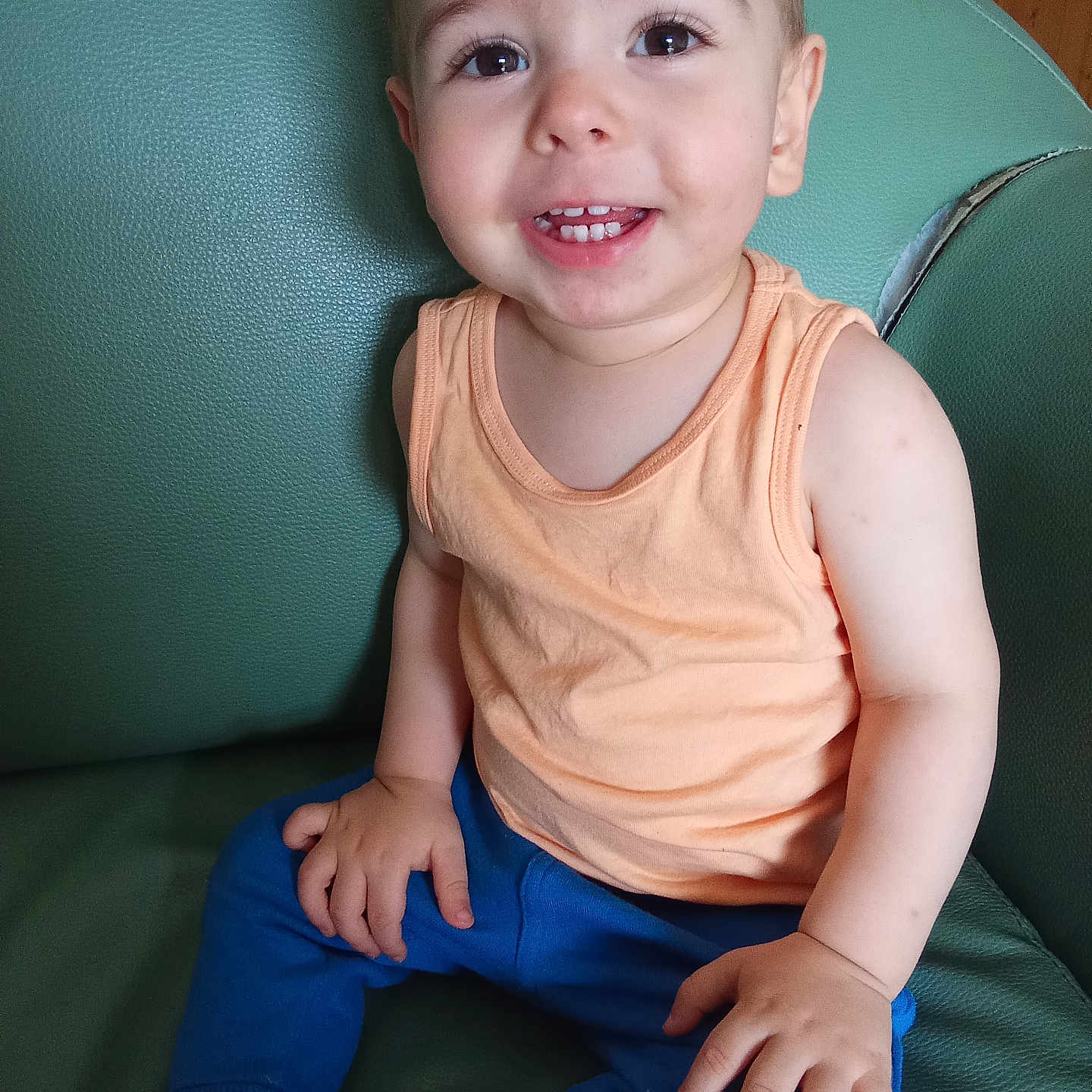 Tiago a rejoint le concours — aidez-le/la à gagner de superbes lots ! baby, blue_pants, casual_clothing, child, cute, face, foot, furniture, green_chair, hand, happy, indoor, person, portrait, sitting, skin, smiling, tank_top, toddler, young_child