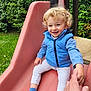 blue_vest, casual_clothing, child, curly_hair, daylight, fun, grass, greenery, hand_holding, happy, outdoor, park, person, pink_slide, play, playground, slide, smiling, sneakers, toddler