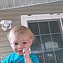 toddler, child, smiling, blonde_hair, blue_shirt, portrait, outdoor, porch, sliding_door, window, house, railing, person, happy, face, casual_clothing, daylight, cute, young_child, playful