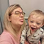 woman, child, toddler, glasses, blonde_hair, long_hair, indoor, smile, playful, tongue_out, person, holding, patterned_clothing, happy, casual, family, portrait, cute, joyful, baby_bottle