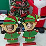 child, christmas_tree, elf_cutout, holiday, indoor, festive, decorations, inflatable_santa, smiling, floor, toy, red, green, playful, happy, celebration, person, christmas, seasonal, fun