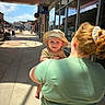 Bjorn joined the competition — help win amazing prizes! baby, bucket_hat, child, daytime, glass_windows, green_shirt, hat, outdoor, parent, person, red_hair, scrunchie, shadow, shopping_area, sidewalk, smile, storefront, sunlight, urban, woman