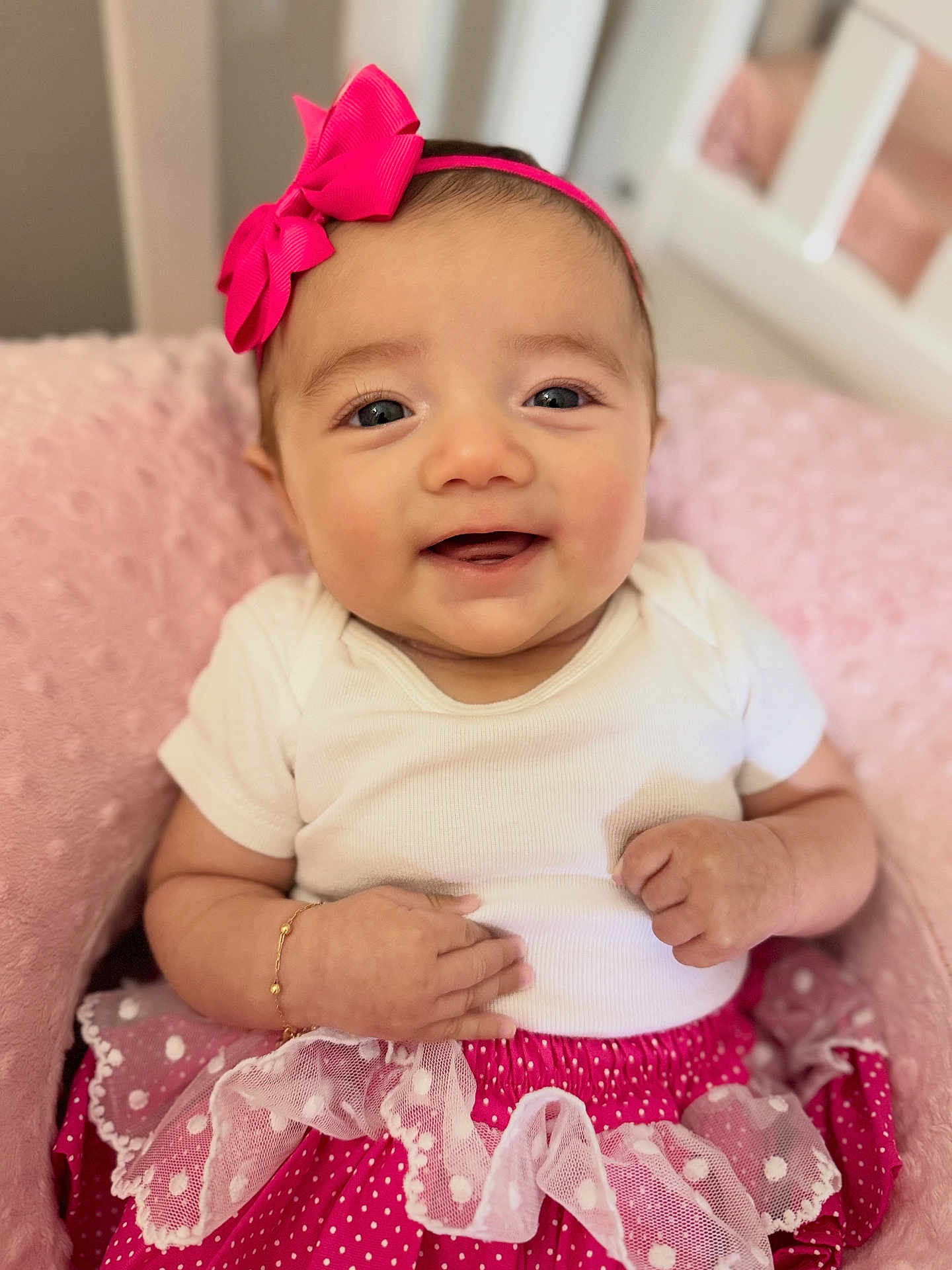 Esther is registered to the contest to win money with this photo: baby, smiling, headband, pink, skirt, polka_dot, white, cushion, sitting, cute, infant, happy, clothing, bracelet, portrait, indoors, soft, child, person, toddler