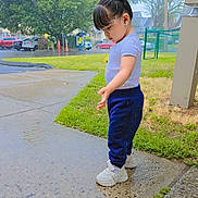 Ashley Pineiros is registered to the contest to win money with this photo: child, toddler, sidewalk, puddle, rain, wet, grass, trees, parked_cars, hair_accessory, white_shoes, blue_pants, white_shirt, outdoor, curious, standing, daylight, urban, nature, person