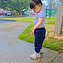 child, toddler, sidewalk, puddle, rain, wet, grass, trees, parked_cars, hair_accessory, white_shoes, blue_pants, white_shirt, outdoor, curious, standing, daylight, urban, nature, person