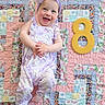 baby, child, smiling, headband, romper, purple, floral_pattern, quilt, patchwork, colorful, number_eight, milestone, happy, infant, cute, lying_down, indoors, playful, celebration, person