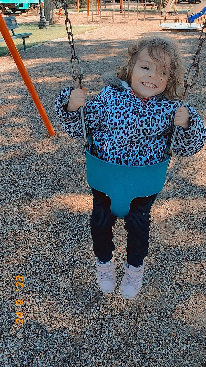 Hazel is registered to the contest to win money with this photo: baby, baby_toddler_clothing, child, city, denim, electric_blue, fun, grass, happy, joy, leisure, outdoor_play_equipment, pattern, person, playground, recreation, sleeve, smile, swing, toddler