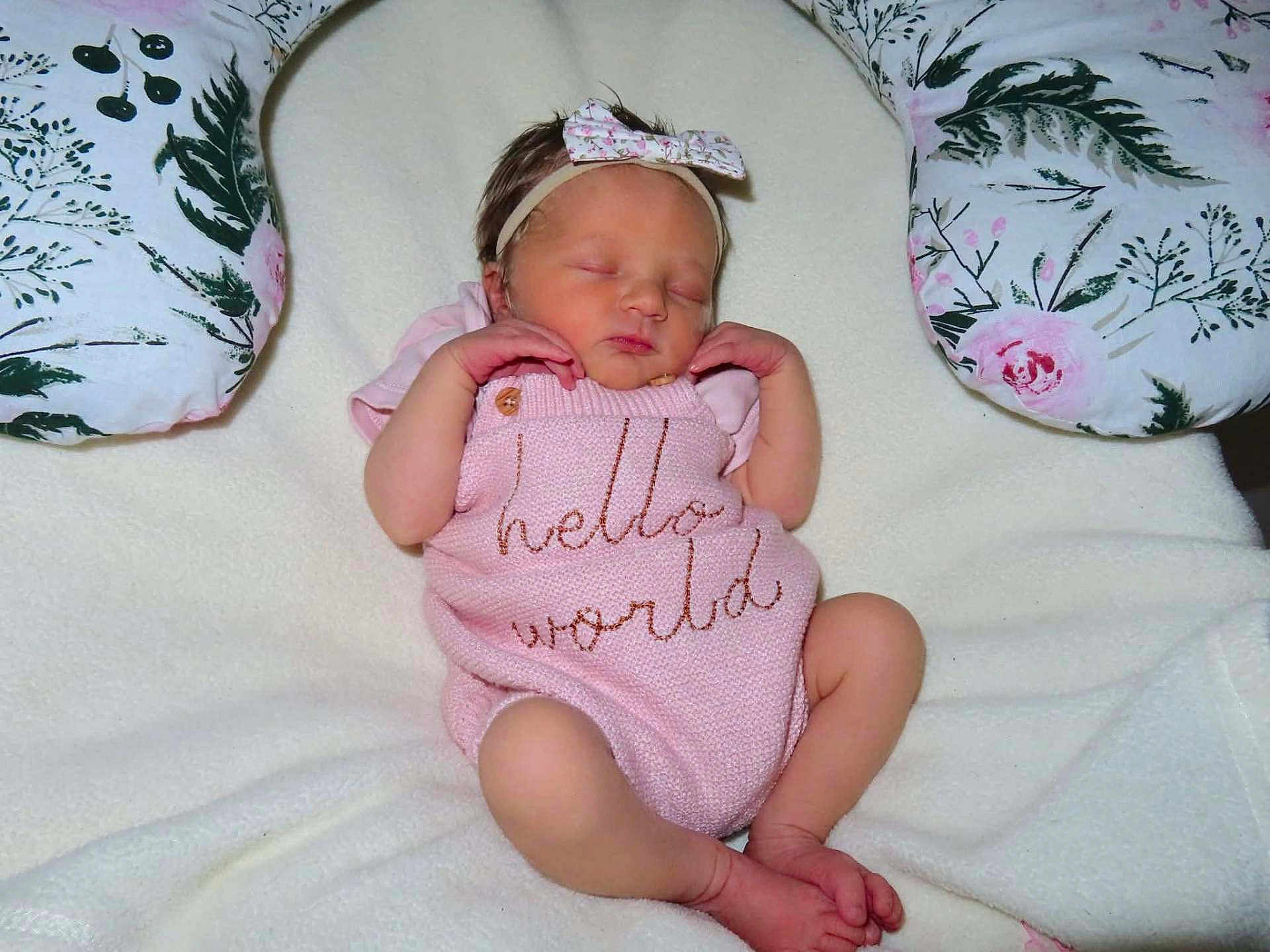 Aria-Jade is registered to the contest to win money with this photo: newborn, baby, sleeping, pink_outfit, headband, floral, blanket, pillow, cute, infant, soft_texture, peaceful, resting, small_hands, small_feet, indoors, portrait, child, knitted_clothing, cozy