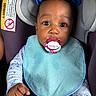 Amirah is registered to the contest to win money with this photo: baby, child, pacifier, car_seat, bib, blue_bows, infant, clothing, face, hand, person, seatbelt, closeup, portrait, cute, indoors, sitting, young_child, expression, safety