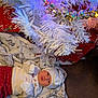 baby, newborn, christmas_tree, holiday_lights, blanket, red_pants, white_hat, festive_clothing, carpet, silver_beads, gift_wrap, indoor, holiday_decor, infant, cute, sleeping_baby, christmas_theme, soft_texture, holiday_spirit, cozy