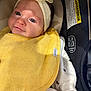 baby, infant, headband, flower, yellow_bib, car_seat, clothing, cute, face, child, portrait, small_hand, white_outfit, black_pattern, seatbelt, safety, indoor, closeup, skin, adorable
