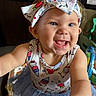 baby, child, infant, smiling, happy, portrait, close_up, face, blue_eyes, bow, headband, dress, cartoon_pattern, colorful_clothing, indoor, seated, toy, chair, playful, photography