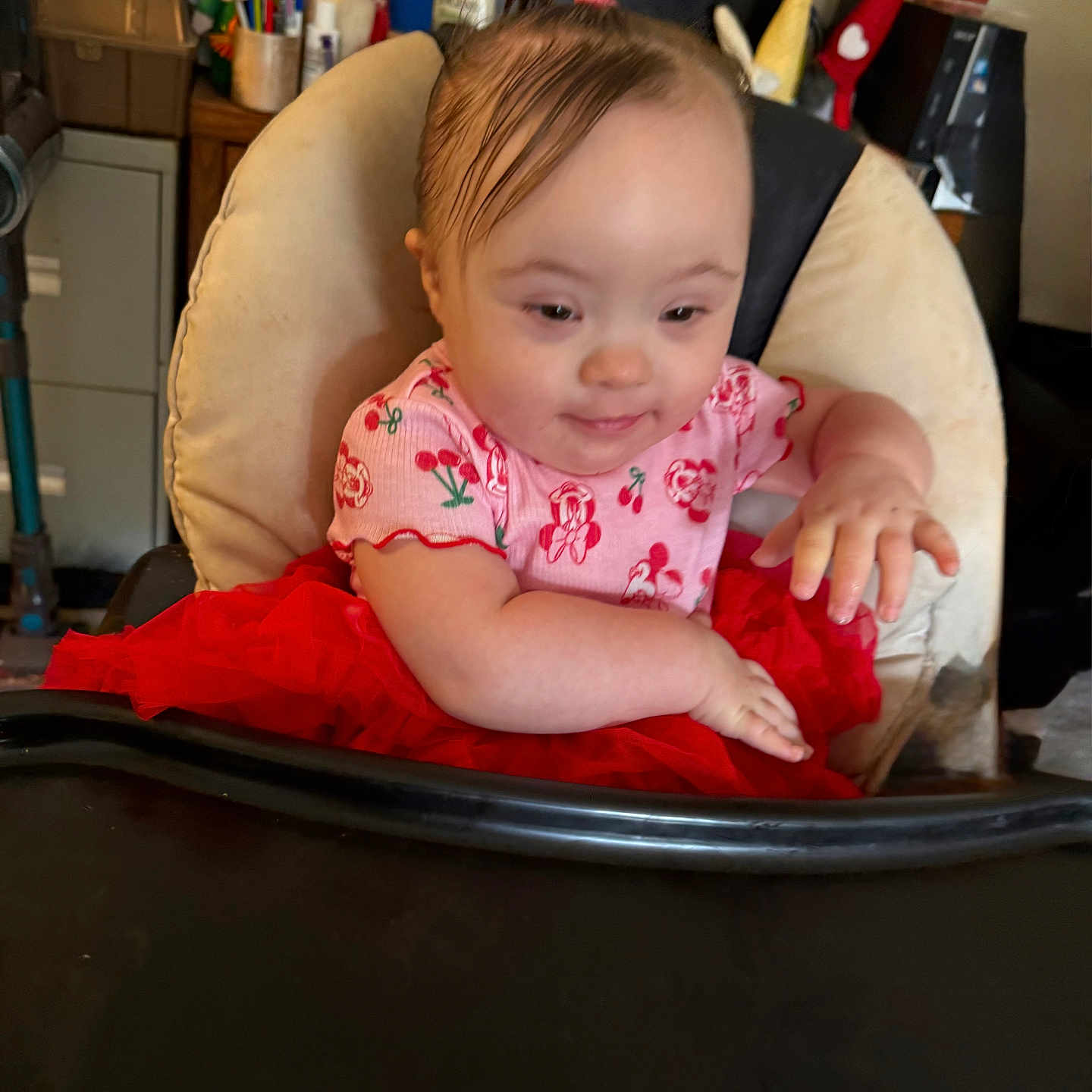 Freya joined the competition — help win amazing prizes! baby, child, infant, portrait, smiling, sitting, high_chair, pink_outfit, red_skirt, floral_pattern, baby_clothing, indoors, home, furniture, cushion, office, desk, computer_monitor, toys, photography