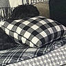 dog, black_dog, pillow, checkered_pattern, blanket, couch, furniture, indoor, cozy, fabric, texture, soft, pet, resting, camouflage, home, comfort, quiet, relaxation, animal