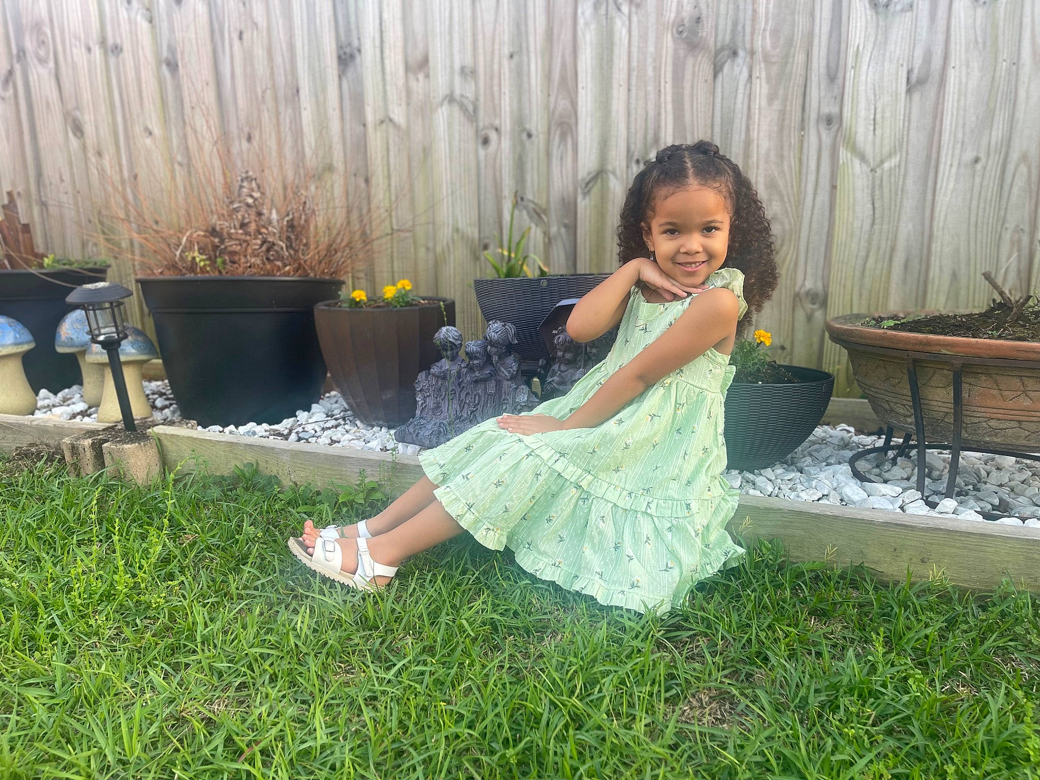 Maliyah is registered to the contest to win money with this photo: child, dress, flash_photography, flowerpot, foot, fun, garden, grass, grass_family, happy, human_leg, joy, leisure, people_in_nature, person, plant, sandal, shrub, sitting, smile