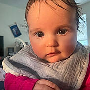 Rosie is registered to the contest to win money with this photo: baby, child, face, hands, pink_clothing, bib, indoor, portrait, curly_hair, closeup, expression, person, infant, cute, young, skin, eyes, hand_gesture, soft_light, home