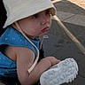 toddler, child, hat, bucket_hat, blue_clothing, sneaker, shoe, stroller, outdoor, pavement, side_view, sunlight, young_child, casual, summer, footwear, curious, baby, person, cute