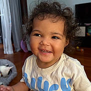Raya joined the competition — help win amazing prizes! toddler, child, curly_hair, smiling, indoor, tshirt, happy, person, floor, cat, pet, bed, wooden_floor, cute, portrait, young_child, sitting, home, casual, playful