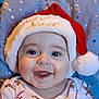 baby, smiling, santa_hat, holiday_clothing, happy, face, child, infant, blue_background, festive, christmas, cute, portrait, indoors, closeup, apparel, red_hat, white_fur, cheerful, tongue