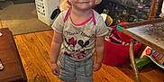Addison is registered to the contest to win money with this photo: toddler, child, indoor, pink_bow, headband, minnie_mouse, tshirt, shorts, shoes, wooden_floor, table, toys, laundry_basket, living_room, smiling, person, furniture, cute, home, standing