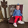 blue_bow, carpet, chair, child, clothing, cute, decorative_arrow, footwear, furniture, happy, indoor, person, portrait, red_pants, smile, toddler, wall_panel, white_shoes, wooden_sign, young_child