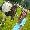 animal, casual_clothing, child, daytime, farm, fence, girl, green_grass, happy, horse, long_hair, nature, outdoor, pasture, petting, rural, summer, sunlight, tree, young