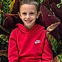 child, boy, smiling, red_hoodie, nike, plant, leaves, green, burgundy, nature, portrait, outdoor, happy, casual_clothing, face, person, young, sitting, photography, background