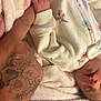 baby, infant, hand, tattoo, blanket, onesie, sleeping, floral_pattern, skin, fingers, cuddle, comfort, soft_texture, closeup, human, rest, peaceful, warmth, parent, bond
