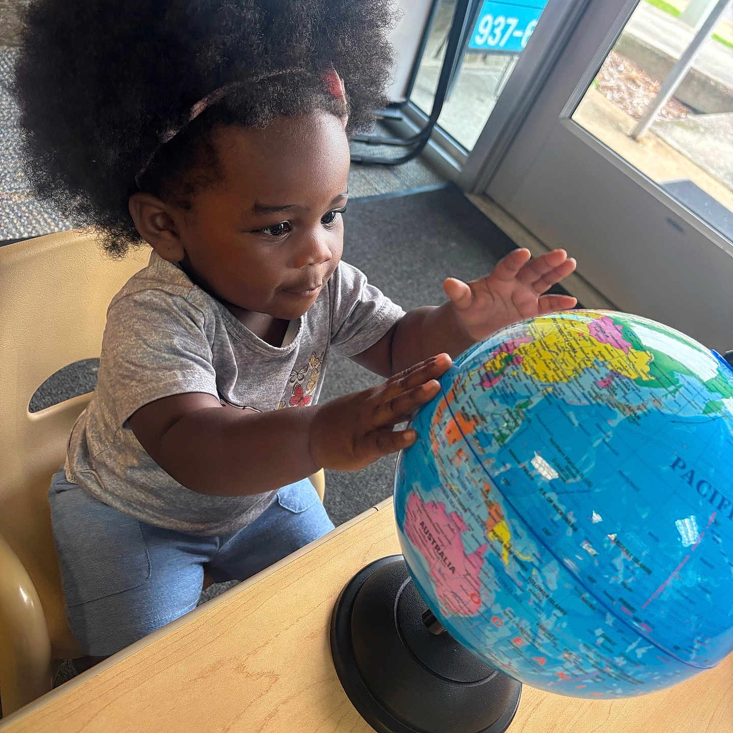 Kasizia is registered to the contest to win money with this photo: afro_hair, blue_pants, chair, child, clothing, curious, door, exploration, globe, hands, indoor, natural_light, person, playful, seated, short_sleeve, table, toddler, window, young_child